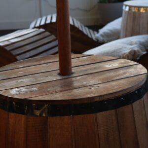 Natural wood beer barrel stool with parasol stand opening and dark metal bands.