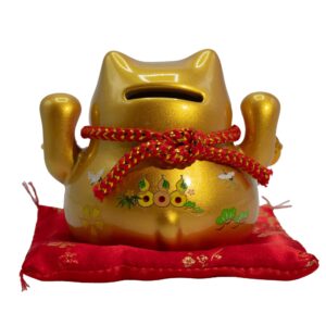 Gold ceramic money cat bank on a red patterned cushion, perfect for home decor.