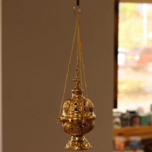 Hanging brass incense burner with intricate engravings and a cross finial.