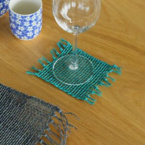 Handwoven turquoise seagrass coasters with fringe detailing for table decor.