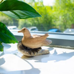 Hand-carved duck resting on a natural wood base, showcasing organic textures.